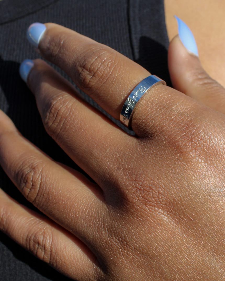 A hand resting on the chest, wearing an engraved band.