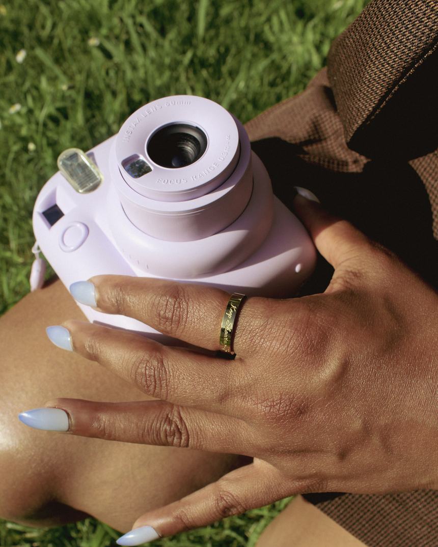 Sitting on the grass with an instant camera, wearing a worn by you band.