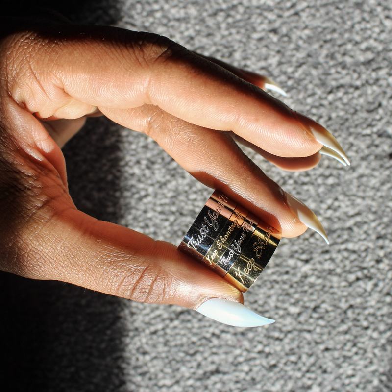 Begin Again ring in gold, held between finger and thumb.