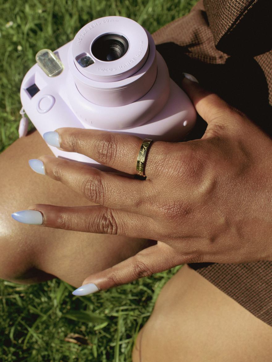A hand resting on an instant camera, wearing a gold band engraved Keep Showing Up.