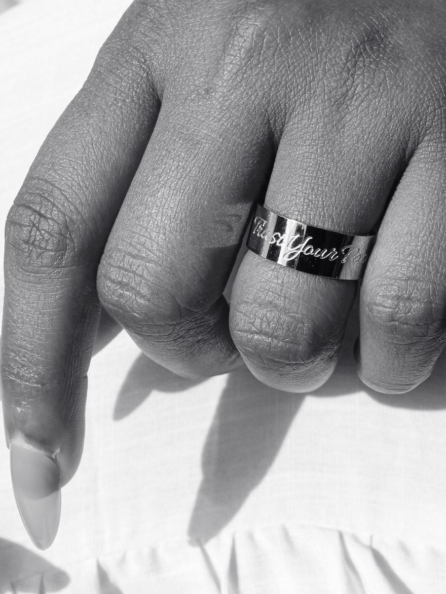 Black and white close-up of a silver band engraved Trust Your Pace.