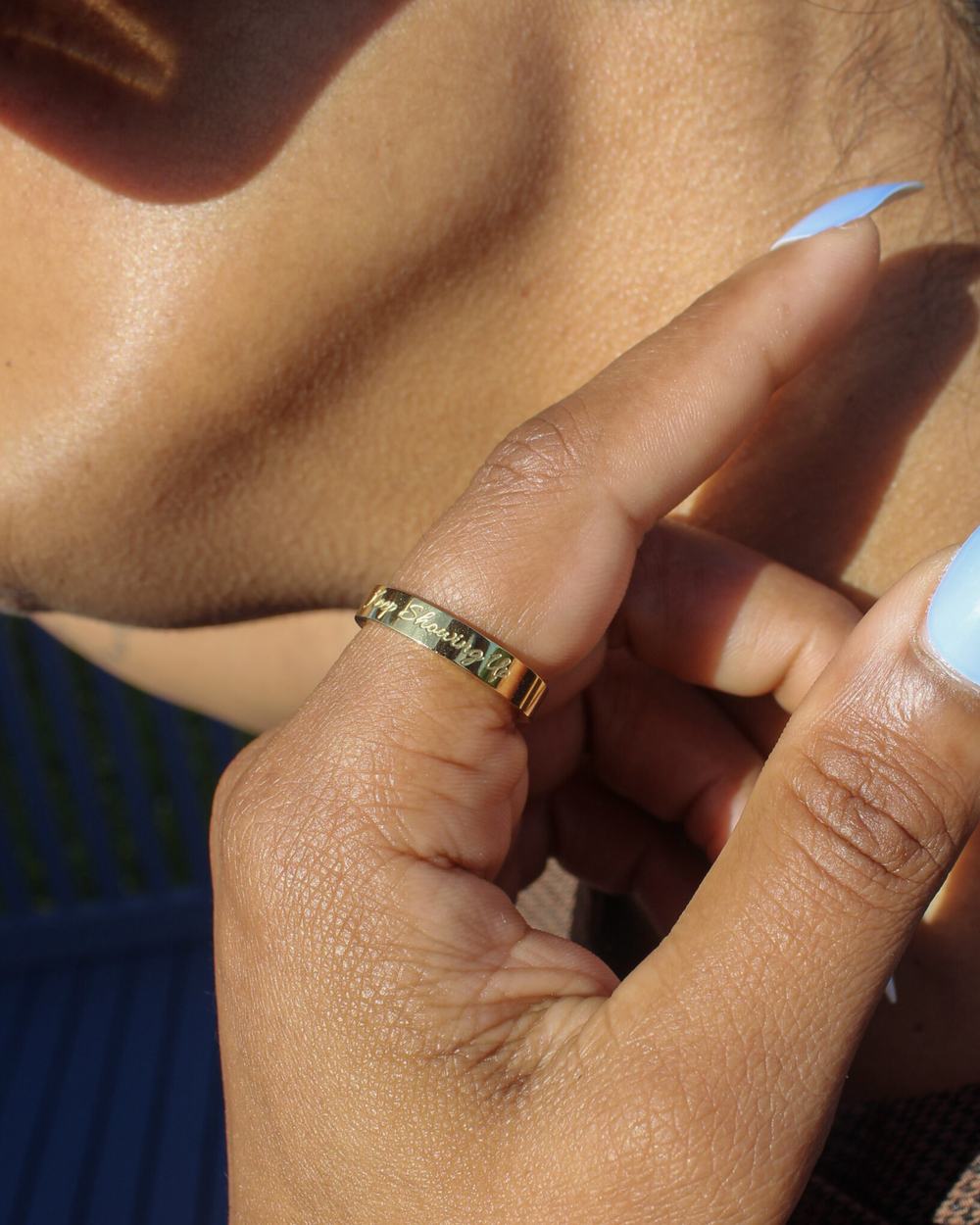 A gold Keep Showing Up band worn on the ring finger, hand raised to the ear.