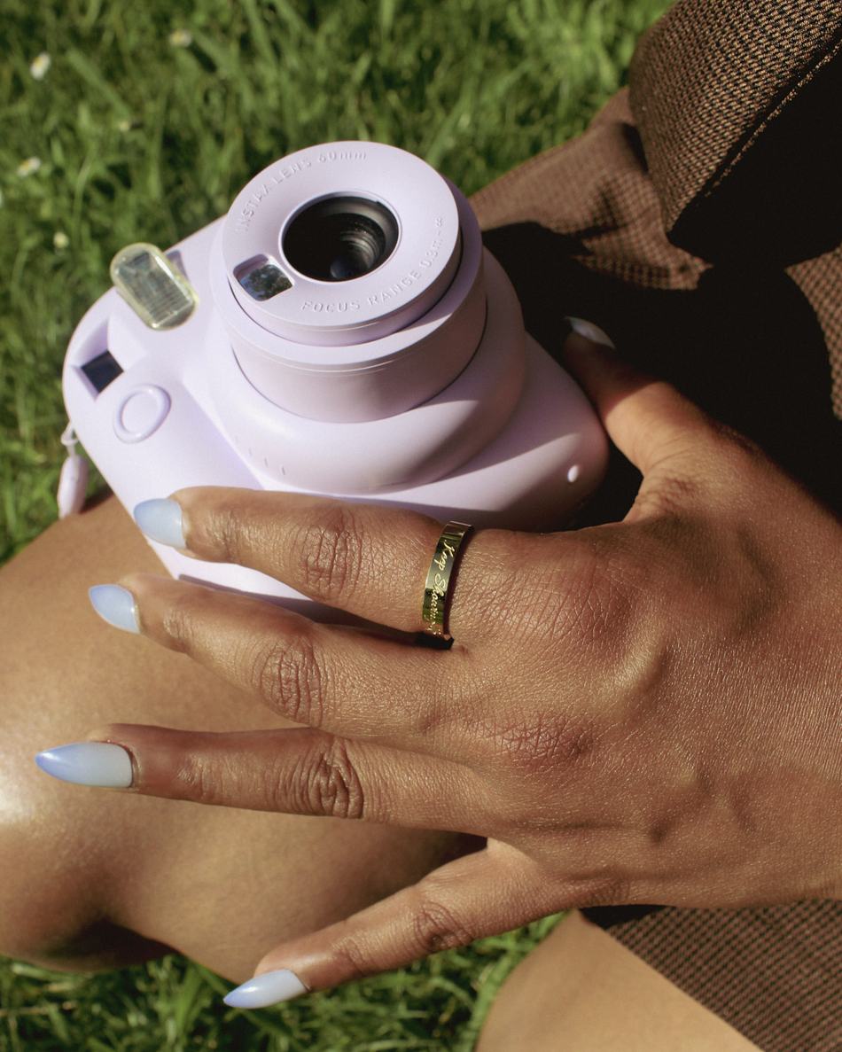 Sitting on the grass with an instant camera, wearing a worn by you band.